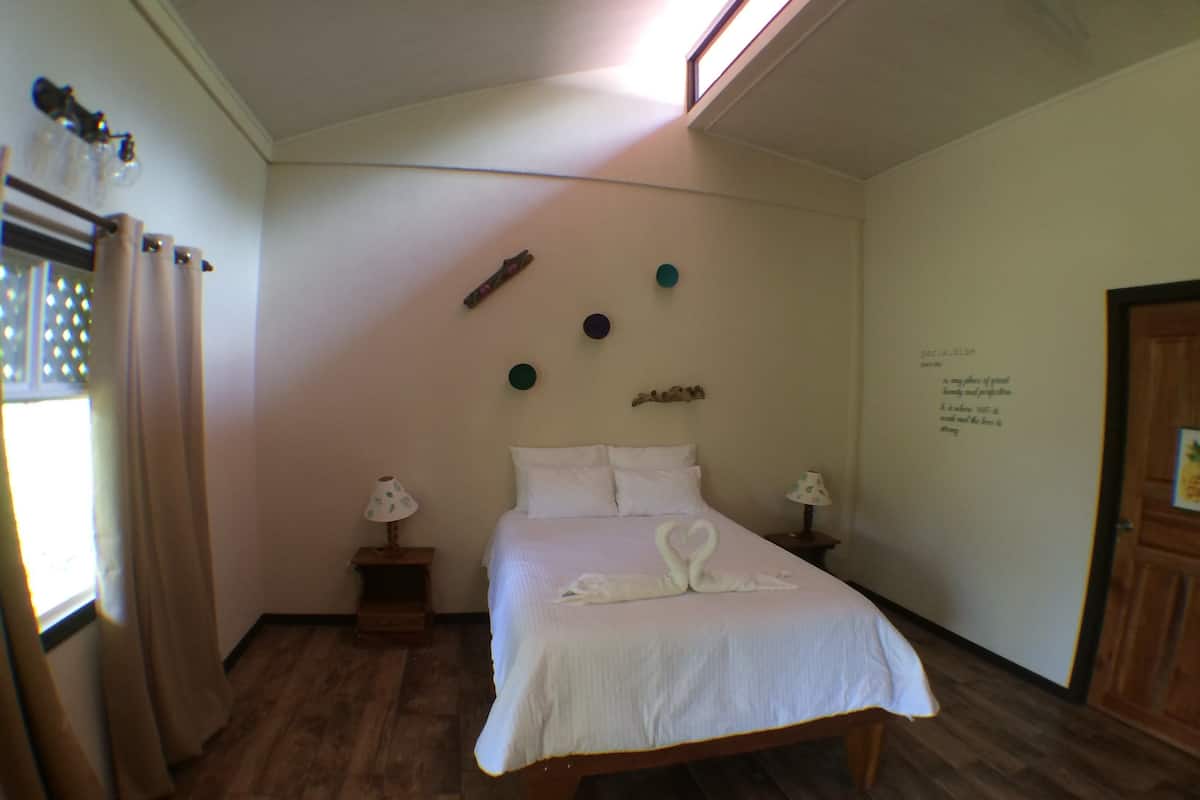 A bedroom with a wooden bed, two bedside tables with lamps, a window with curtains, and a wall with decorative items.