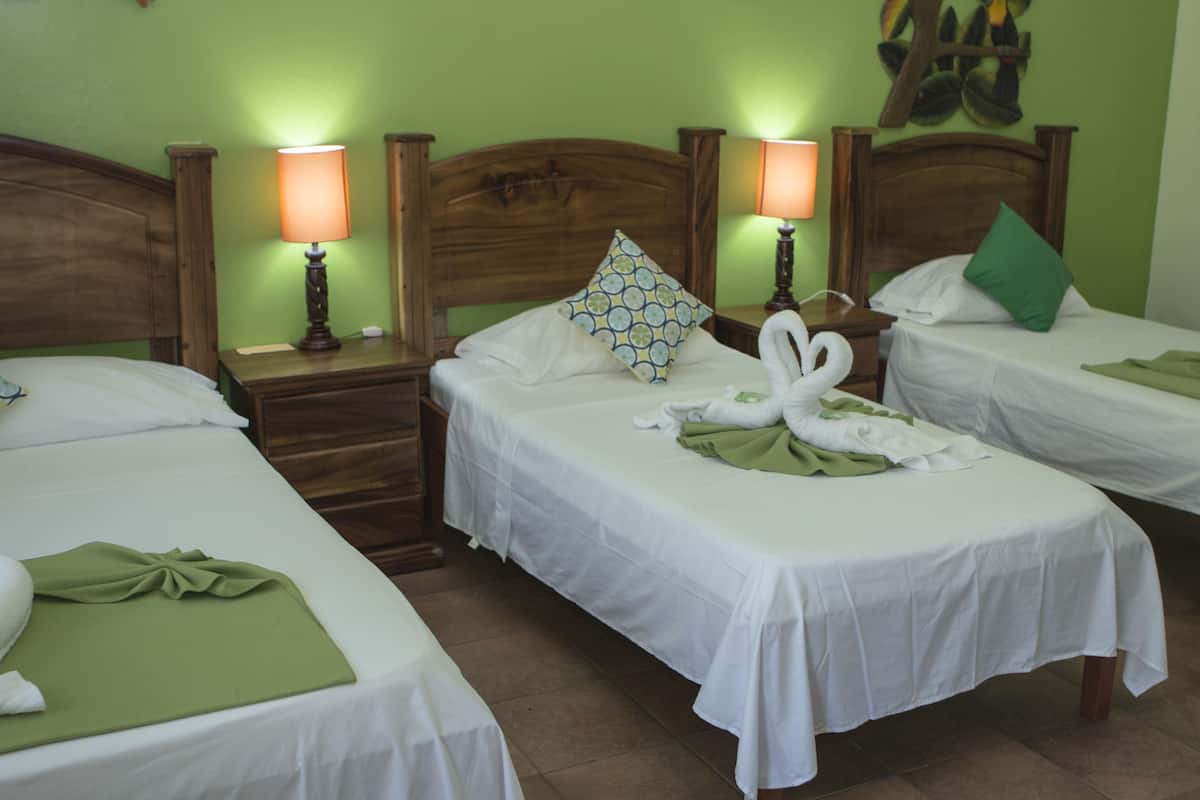 A hotel room with two single beds, each with a wooden headboard, a green pillow, and a white bedspread. There are two bedside lamps and a wall-mounted artwork above the beds.