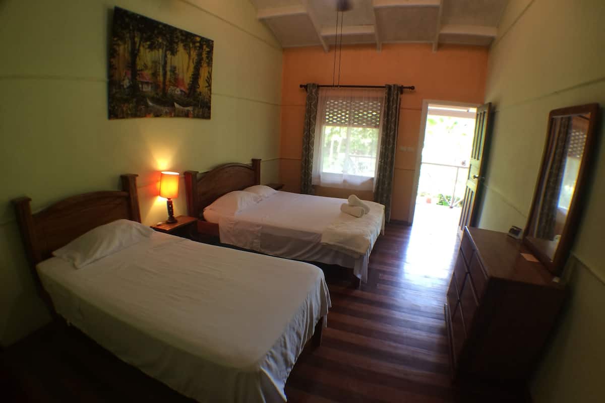 A hotel room with two single beds, a nightstand with a lamp, a painting on the wall, and a window with curtains.