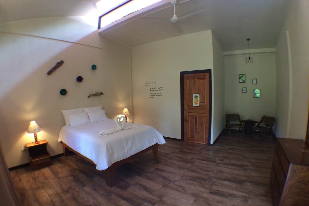 A bedroom with a bed, bedside lamps, a wooden door, and a small seating area with chairs.