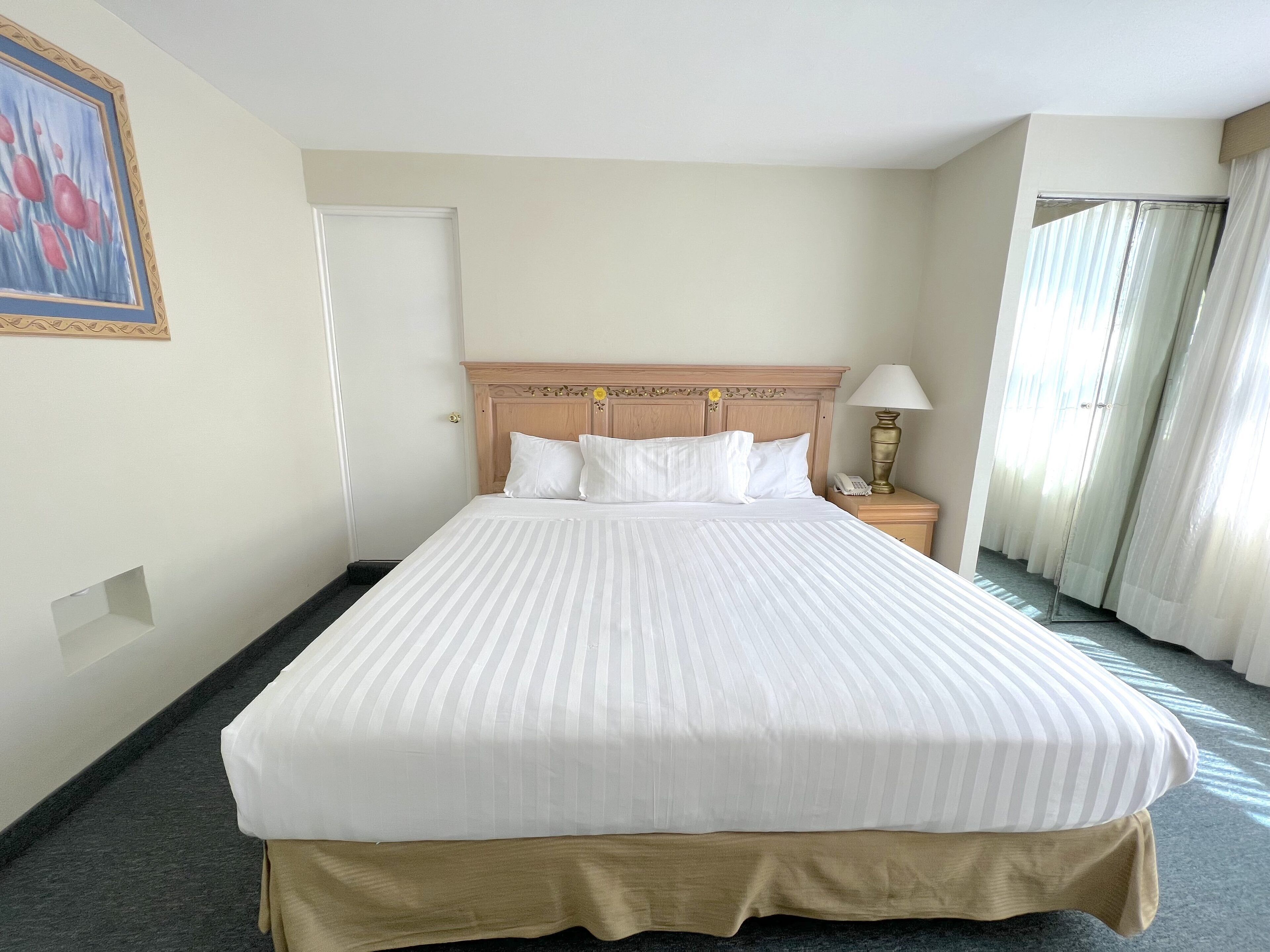 A hotel room with a large bed, a wooden headboard, a bedside table with a lamp, and a door.
