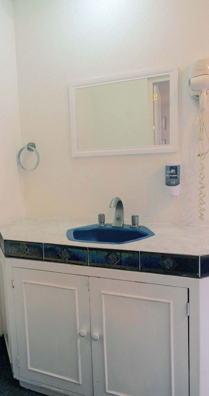 Un baño con tocador blanco, lavamanos azul, espejo y argolla para toallas.