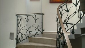 Uma escadaria com corrimão de metal, degraus bege e duas pinturas nas paredes.