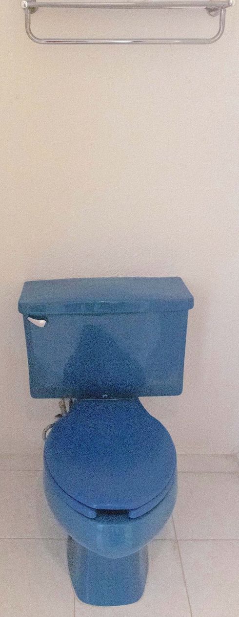 Un gabinetto blu con serbatoio e sedile, posato su un pavimento piastrellato.