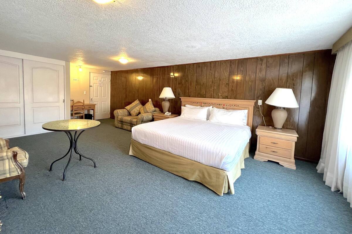 A hotel room with a large bed, a small round table, a chair, and a wooden accent wall.