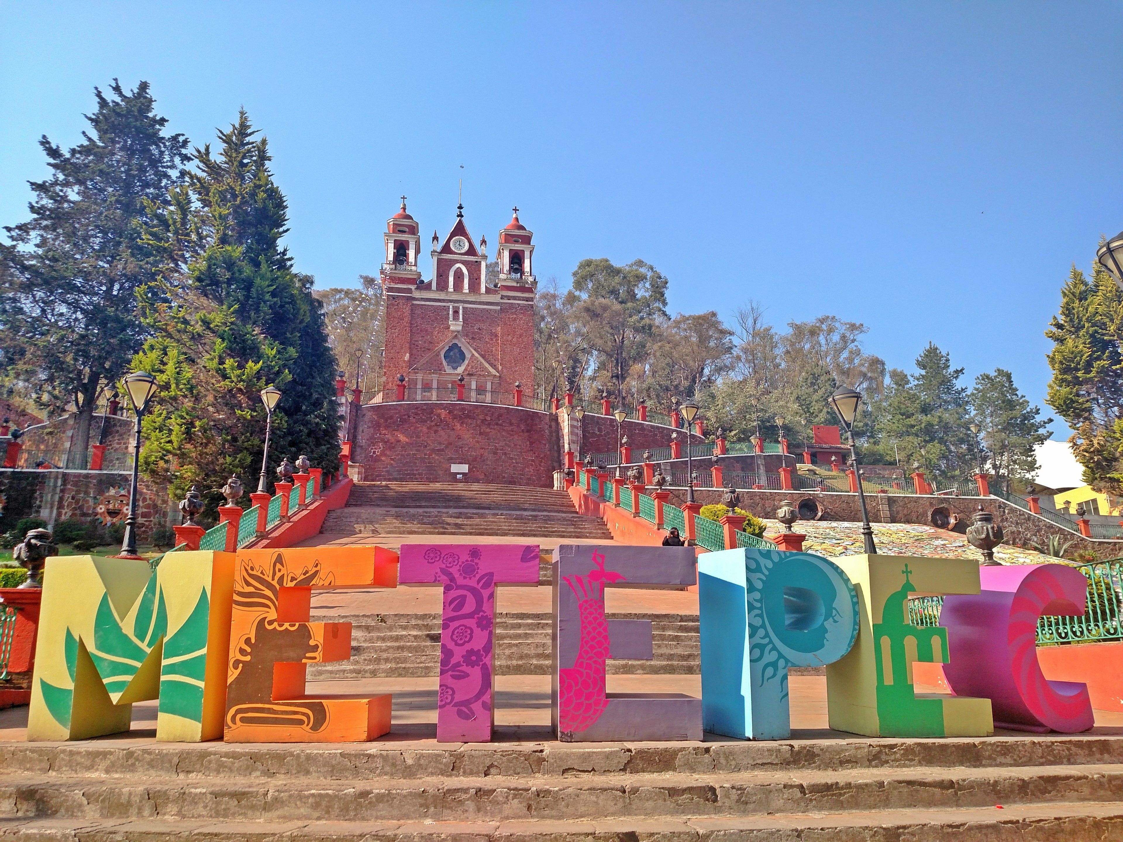 A staircase leading to a church with a bell tower, surrounded by colorful letter sculptures.