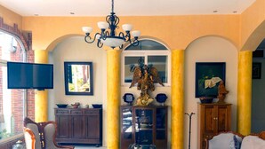 Uma sala de estar ampla, com um candelabro, uma televisão e uma janela grande.