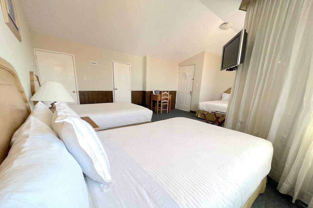 A hotel room with two beds, a desk, a chair, a TV, and a window with curtains.
