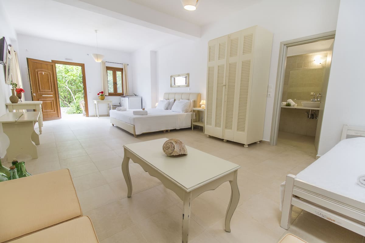 A hotel room with a bed, a table, a sofa, a wardrobe, and a bathroom visible through an open door.