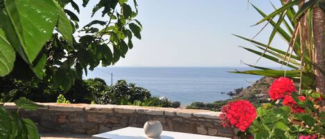 A table with a white vase, a stone wall, and a view of the sea.