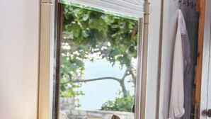 A room with a white vanity, a mirror, a lamp, and a view of outdoor furniture and greenery. - Petrino (Naxos)