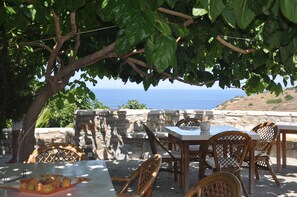 An outdoor seating area with stone walls and wicker chairs, overlooking a coastal view. - Petrino (Naxos)