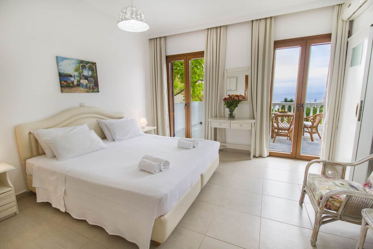 A hotel room with a large bed, a desk, a chair, and a balcony with a view.