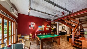 A billiards table in a room with wooden floors, a red wall, and a staircase. - Hotel Boutique Britânico (Gramado)
