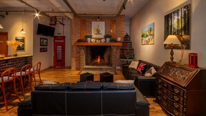 A cozy living room with a fireplace, a sofa, a red telephone booth, and a bar area with stools. - Hotel Boutique Britânico (Gramado)
