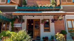 A storefront with a wooden facade, a sign reading "Británico," and a variety of potted plants and flowers in front. - Hotel Boutique Britânico (Gramado)