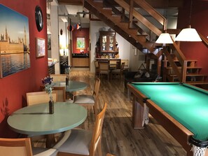 Una sala de billar con mesa de billar, piso de madera y una escalera.