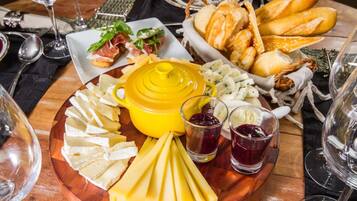 A charcuterie board with various cheeses, bread, and meats, accompanied by wine glasses and a yellow pot.