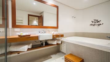 Ein Badezimmer mit großem Spiegel, Waschbecken, Badewanne und einer hölzernen Sitzbank.