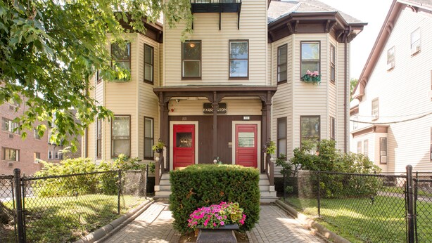 A two-story building with a red door and a sign above it. There is a small garden with flowers in front of the building. - The Farrington Inn (Boston)