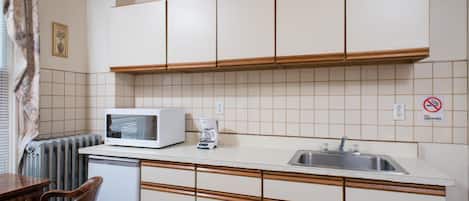 Una cocina compacta con armarios blancos, microondas, cafetera y lavamanos.