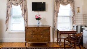 A room with a wooden dresser, a television mounted on the wall, a vase with flowers, and a chair. - The Farrington Inn (Boston)
