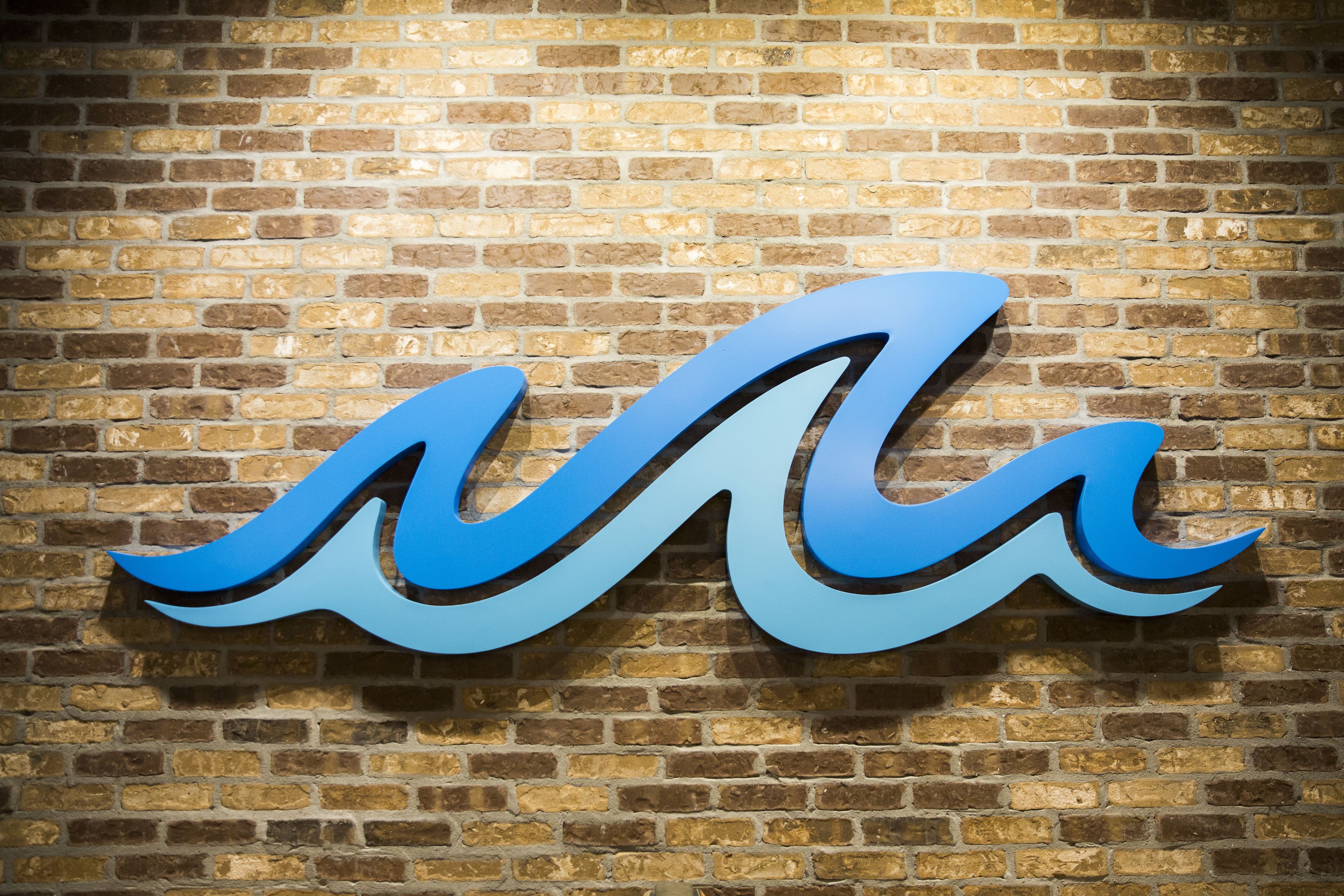 A blue, stylized wave logo on a brick wall.