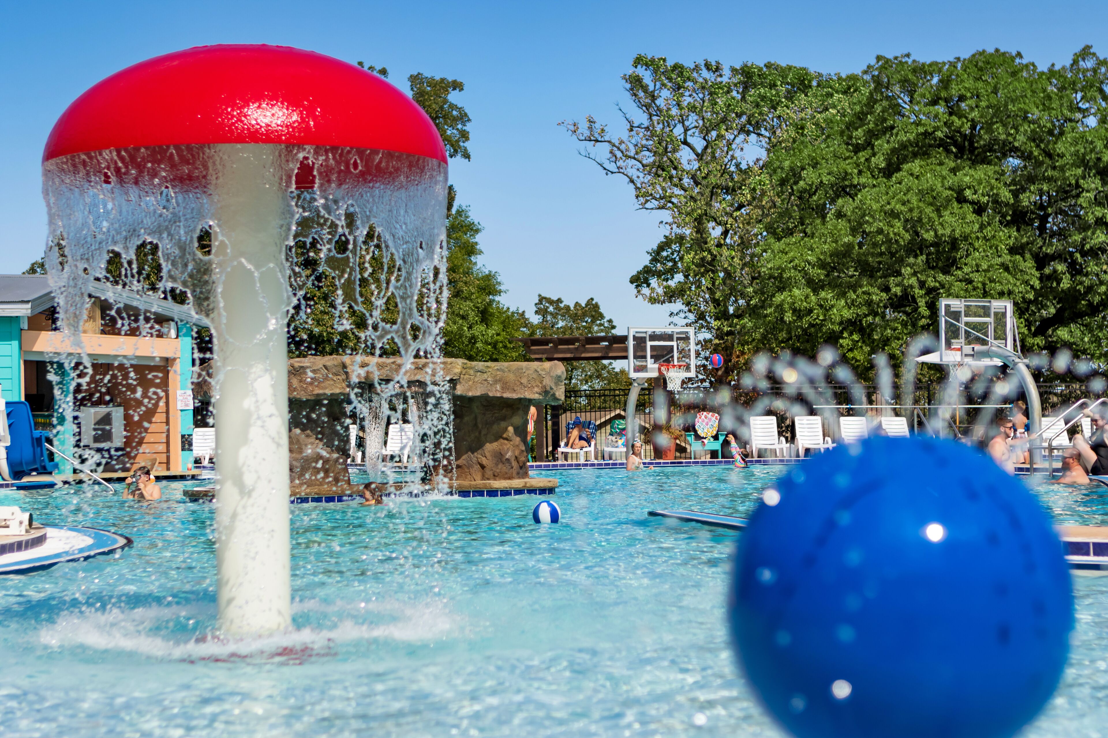 A pool area with a water feature, lounge chairs, and a basketball court.