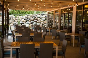 An outdoor dining area with tables and chairs, a stone wall, and string lights. - Bridges Bay Resort (Arnolds Park)