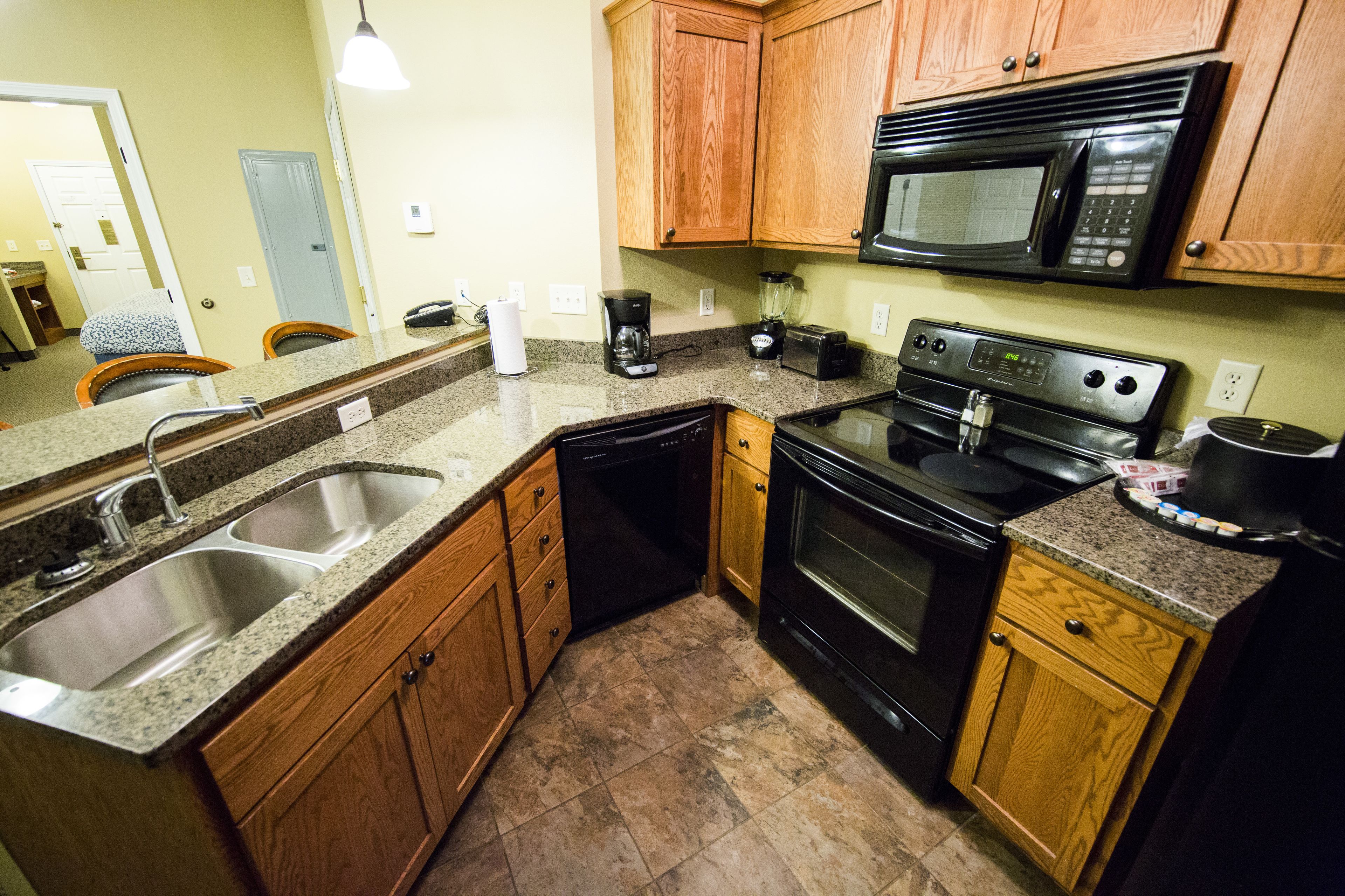 A compact kitchen with wooden cabinets, a stainless steel sink, a black microwave, and a stove.