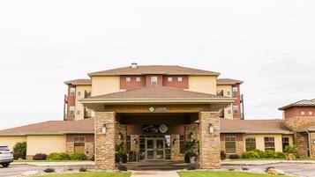 A multi-story building with a covered entrance, stone pillars, and a sign welcoming visitors.