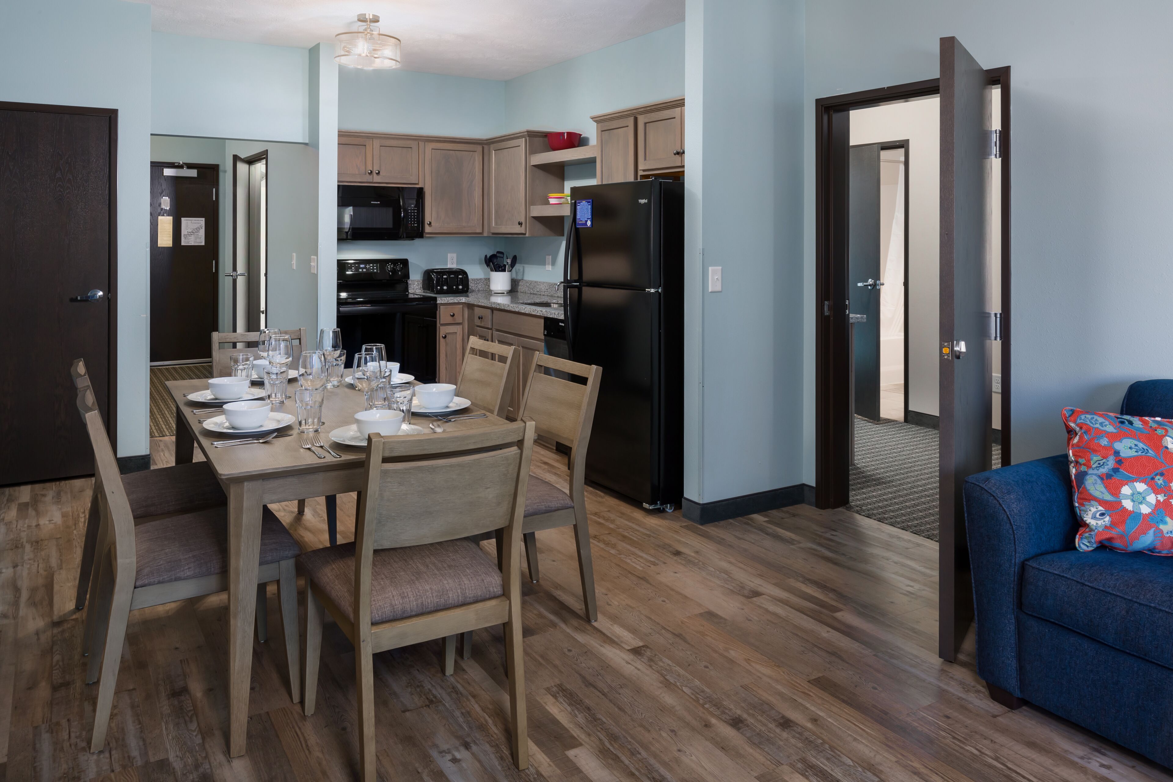 A modern kitchen with wooden cabinets, a black refrigerator, and a dining table set for four.