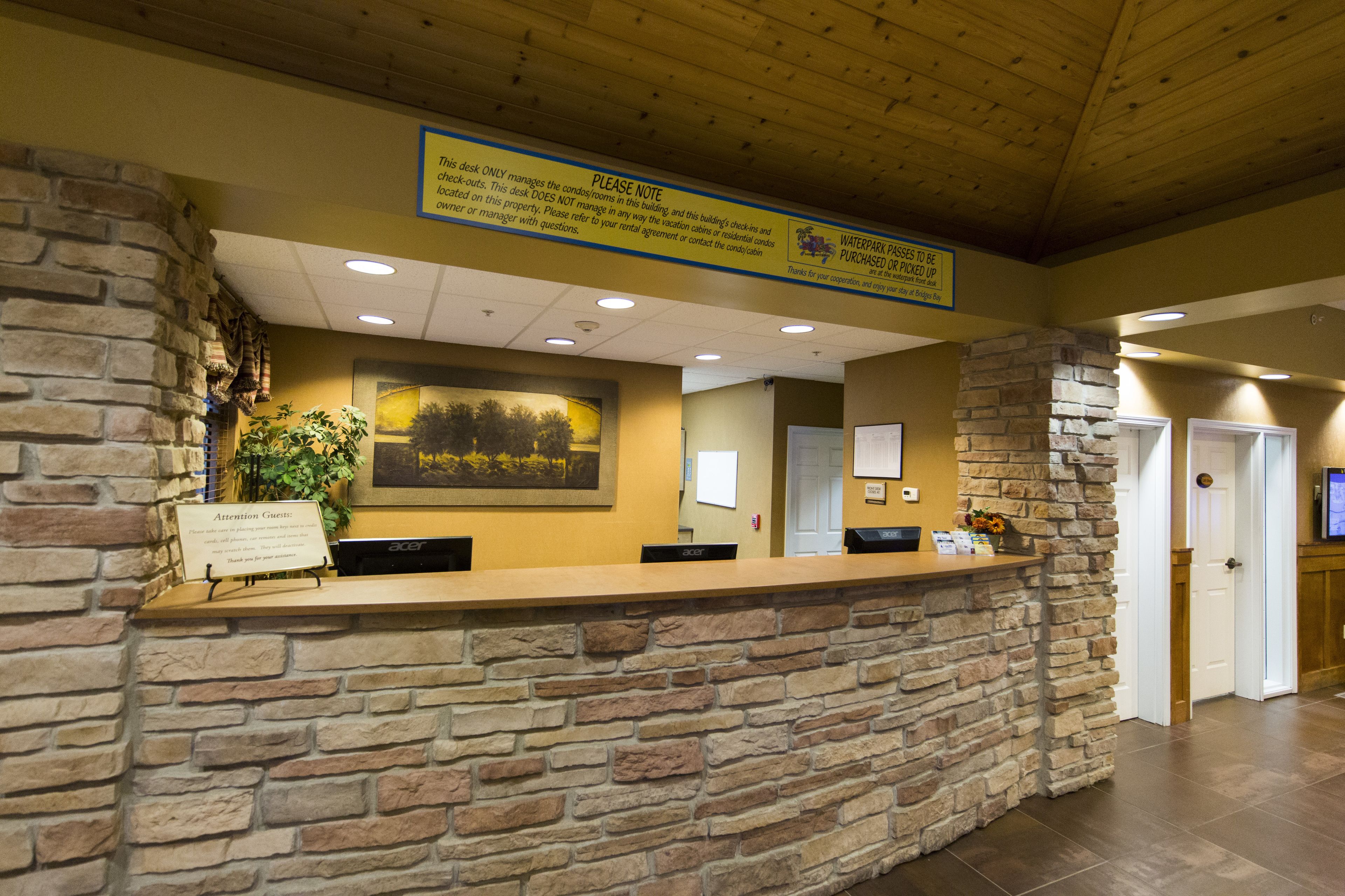 A reception desk with a stone wall, a framed landscape picture, and a sign above stating the desk manages the check-ins.