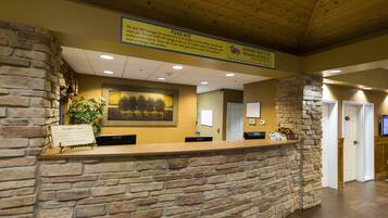 A reception desk with a stone wall, a framed landscape picture, and a sign above stating the desk manages the check-ins.