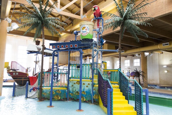 An indoor water park with a pirate ship, palm trees, and a colorful play area.