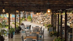 An outdoor cafe with tables and chairs, a stone wall, and hanging lights. - Bridges Bay Resort (Arnolds Park)