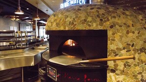 A brick oven pizza oven with a wooden pizza peel, a digital clock, and a neon sign above. - Bridges Bay Resort (Arnolds Park)