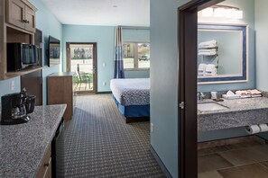 A hotel room with a bed, kitchenette, bathroom, and a view of the outside. - Bridges Bay Resort (Arnolds Park)