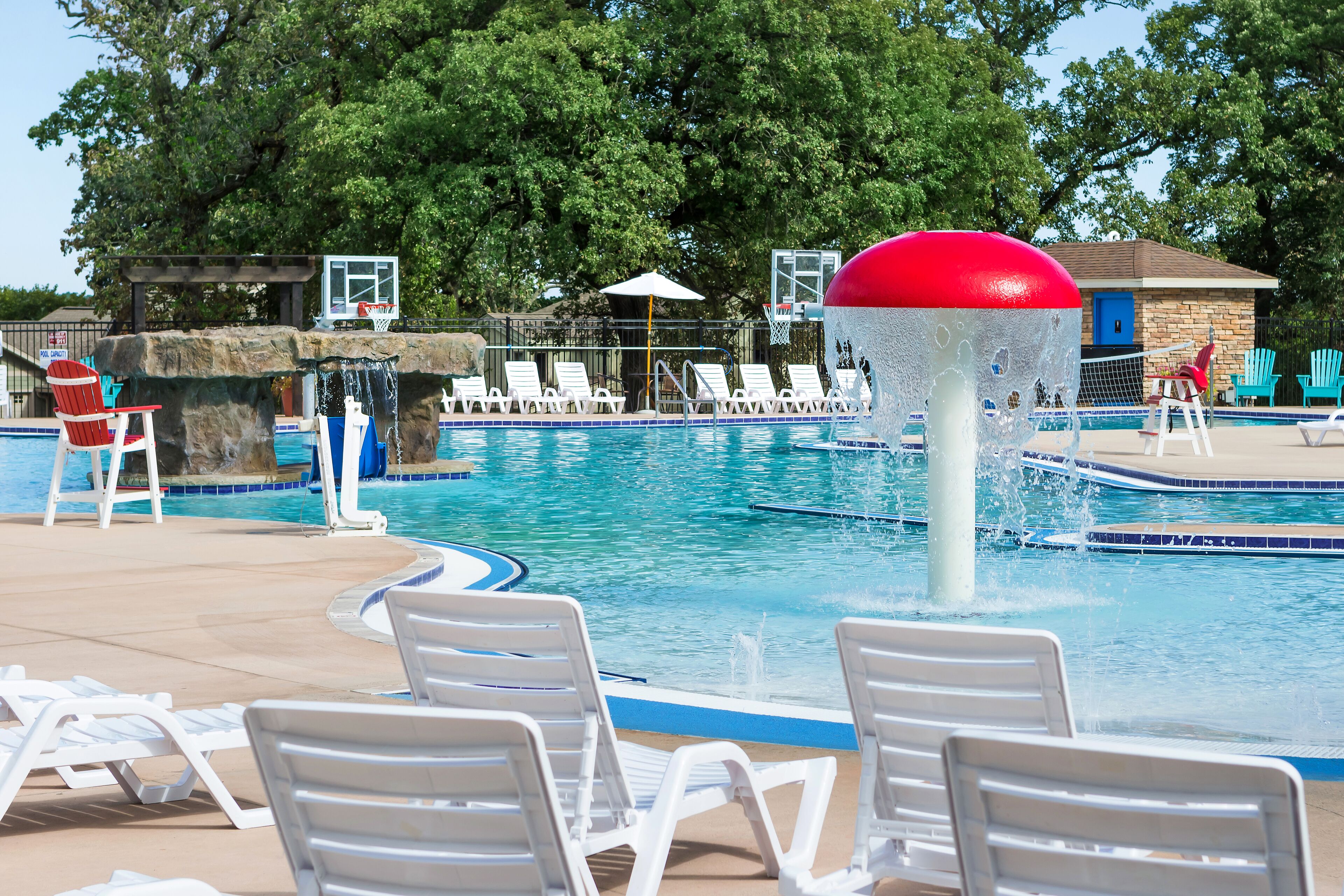 A swimming pool with lounge chairs, a water fountain, and a basketball hoop.