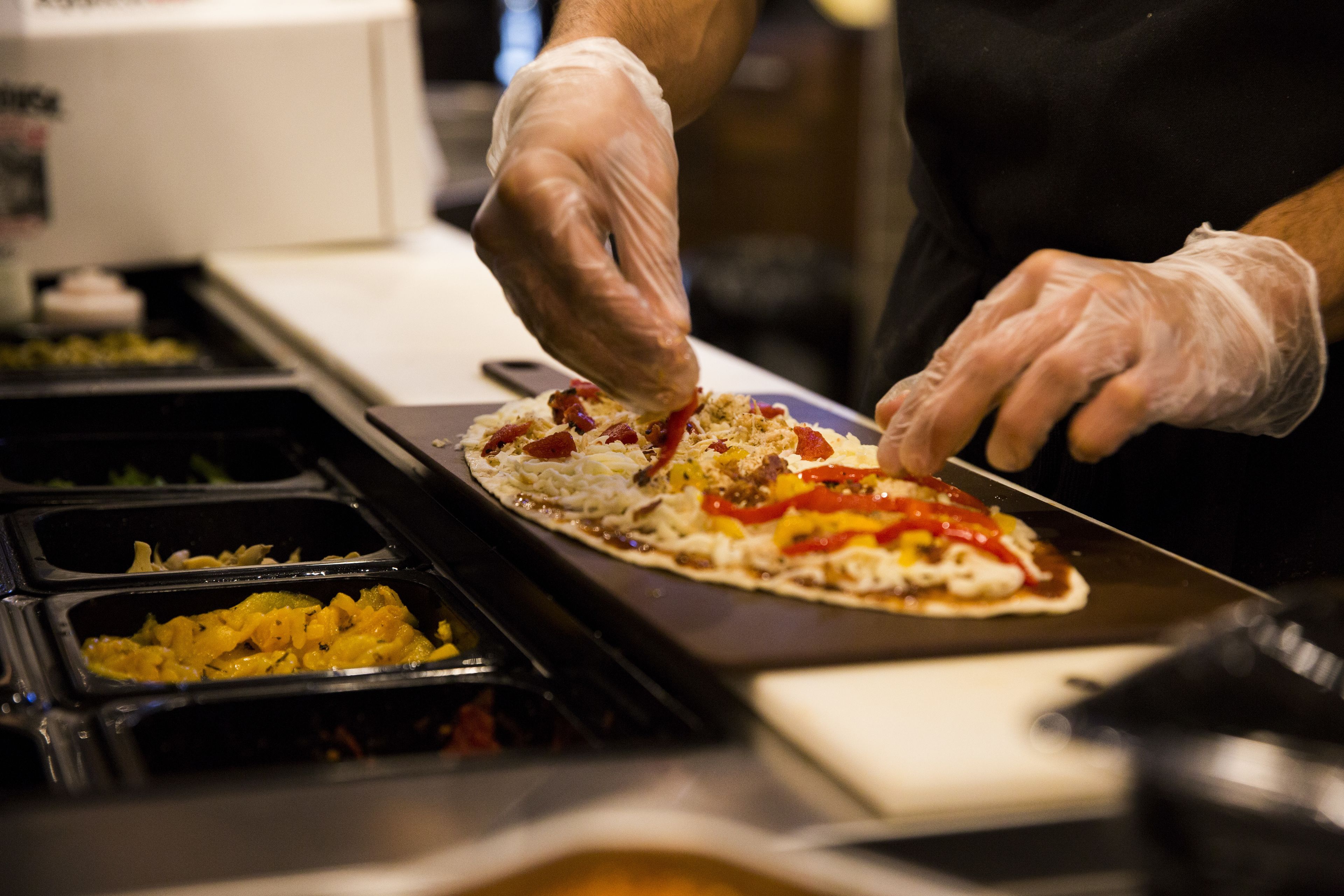 Eine Person bereitet Essen zu, speziell eine Pizza, wobei verschiedene Zutaten in Schalen sichtbar sind.