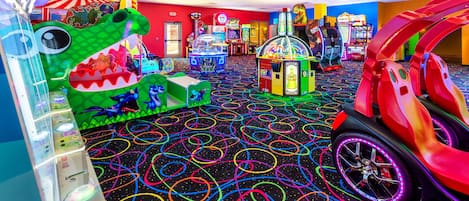 A brightly lit arcade with various gaming machines, a colorful floor design, and a red car-shaped play area.