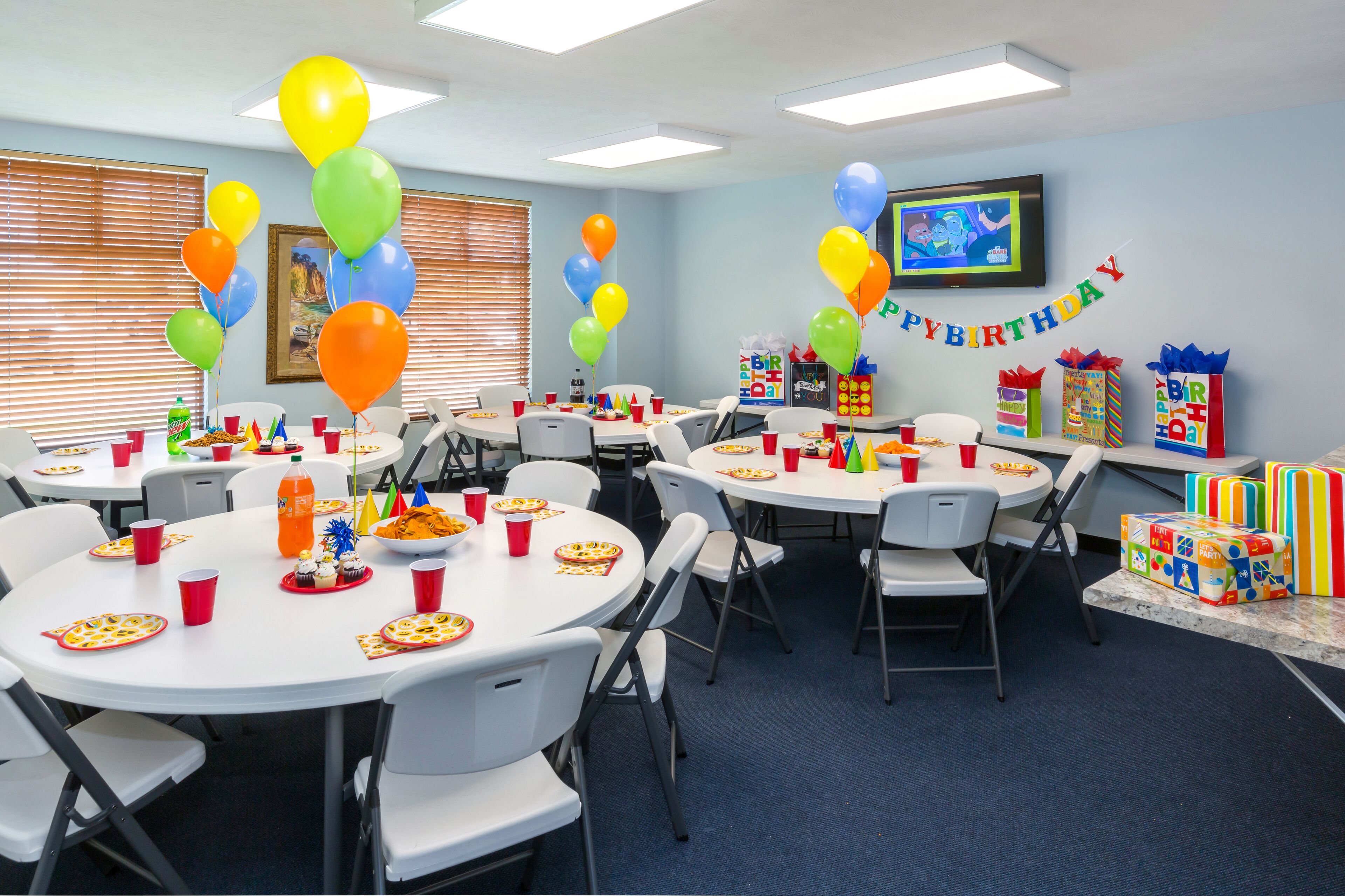 Una habitación con varias mesas dispuestas para una fiesta, globos y cajas de regalo.