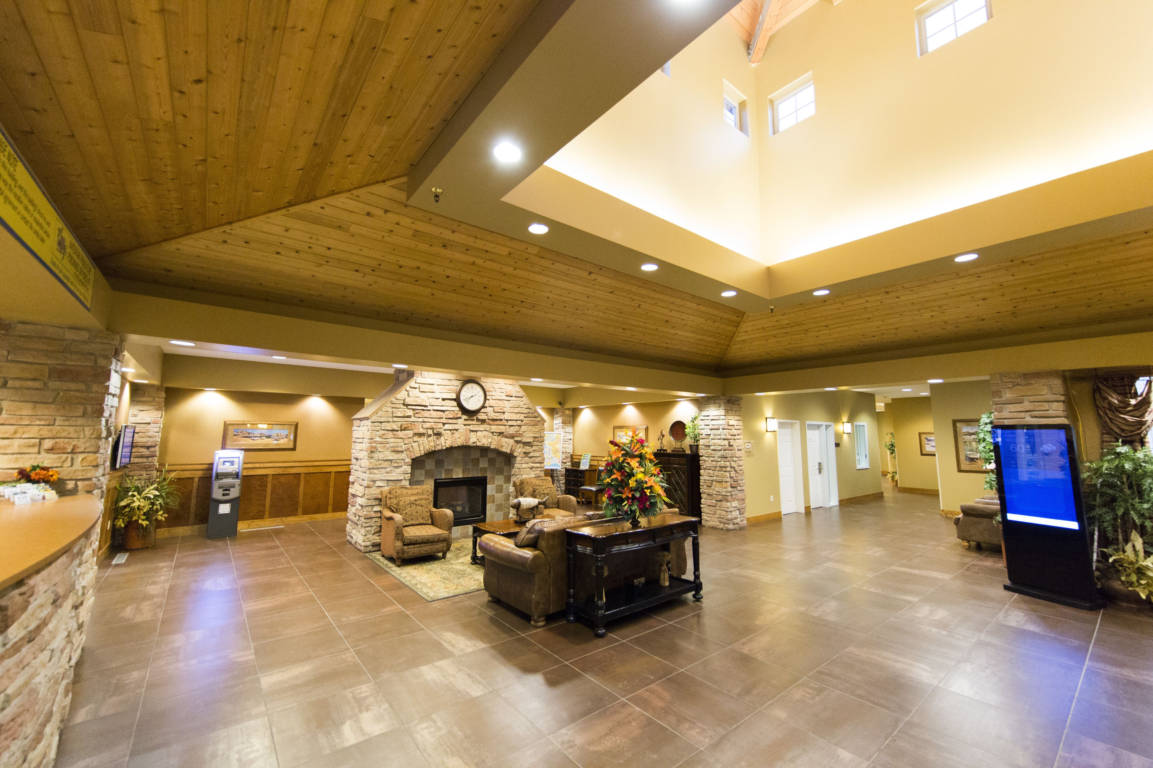 A spacious lobby with a stone fireplace, comfortable seating, a reception desk, and a digital information kiosk.