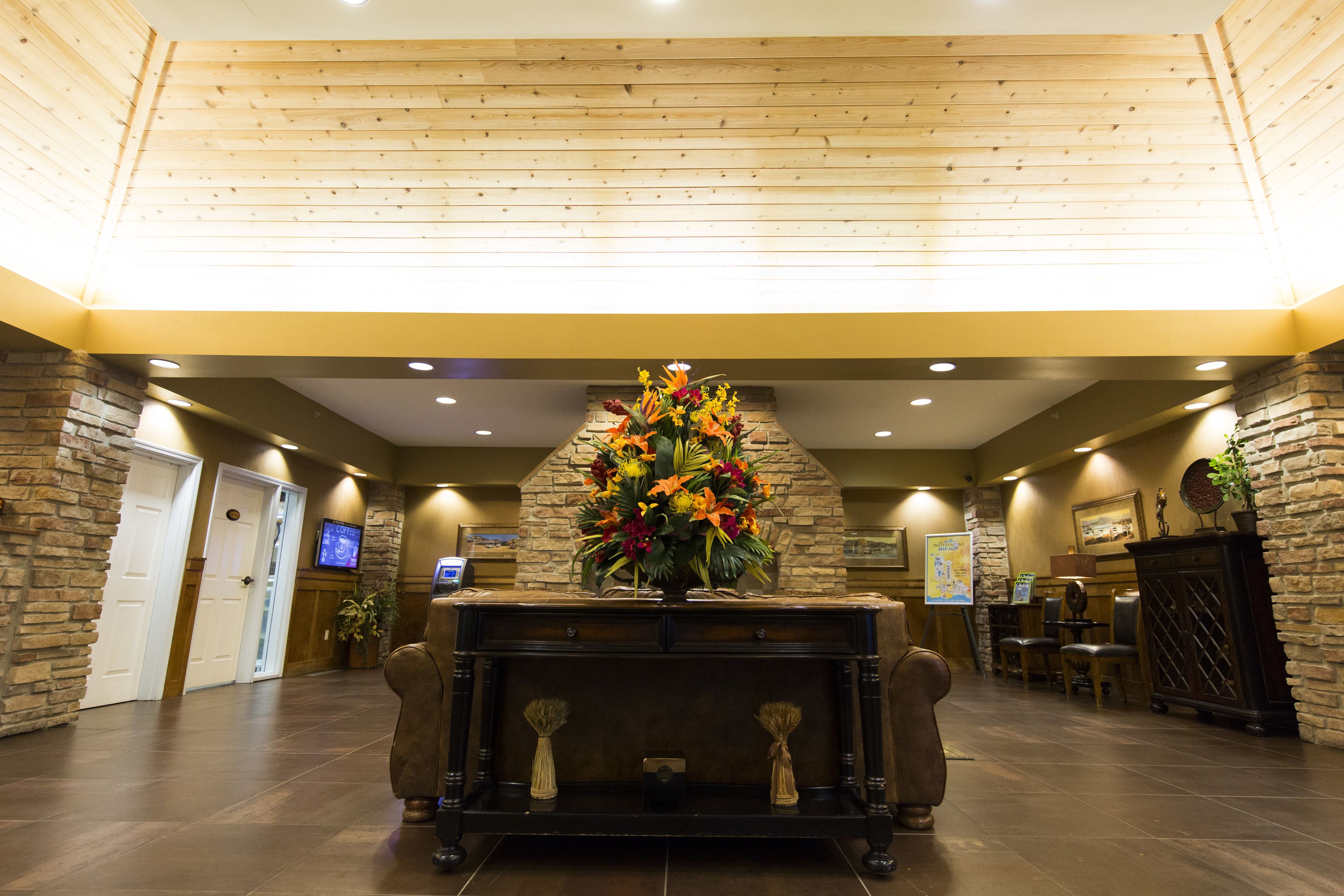 A lobby with a fireplace, stone walls, wooden ceiling, and a television screen.