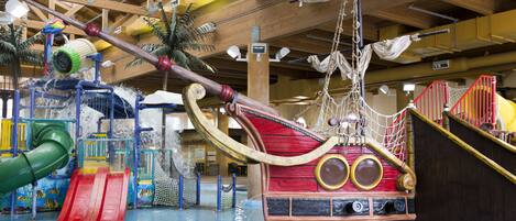 An indoor water park with a pirate ship-themed play area, slides, and a climbing structure.