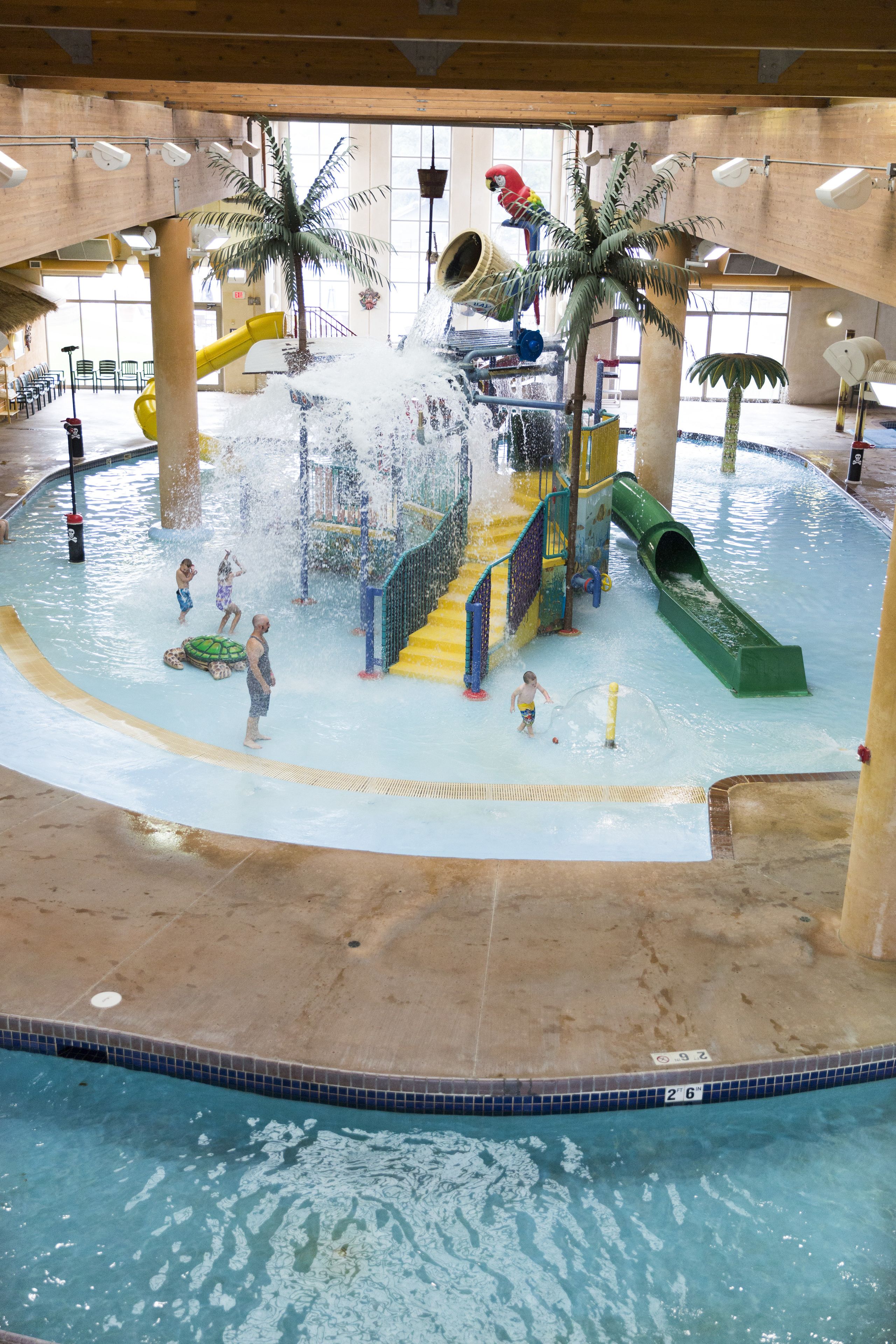 Parque acuático interior con toboganes, fuentes de agua y palmeras.