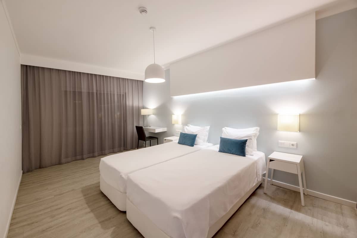 A modern hotel room with a large bed, bedside tables, a desk, and a chair.
