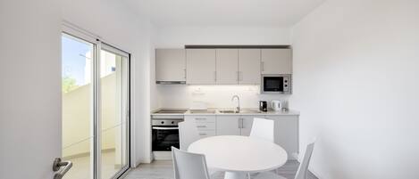 Une cuisine moderne avec des meubles blancs, une table à manger blanche et des chaises. Une porte-fenêtre coulissante donne accès à un espace extérieur.