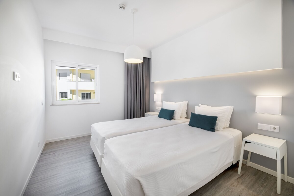 Une chambre d’hôtel moderne avec deux lits, une fenêtre donnant sur un beau paysage, une table de chevet et une lampe fixée au mur.