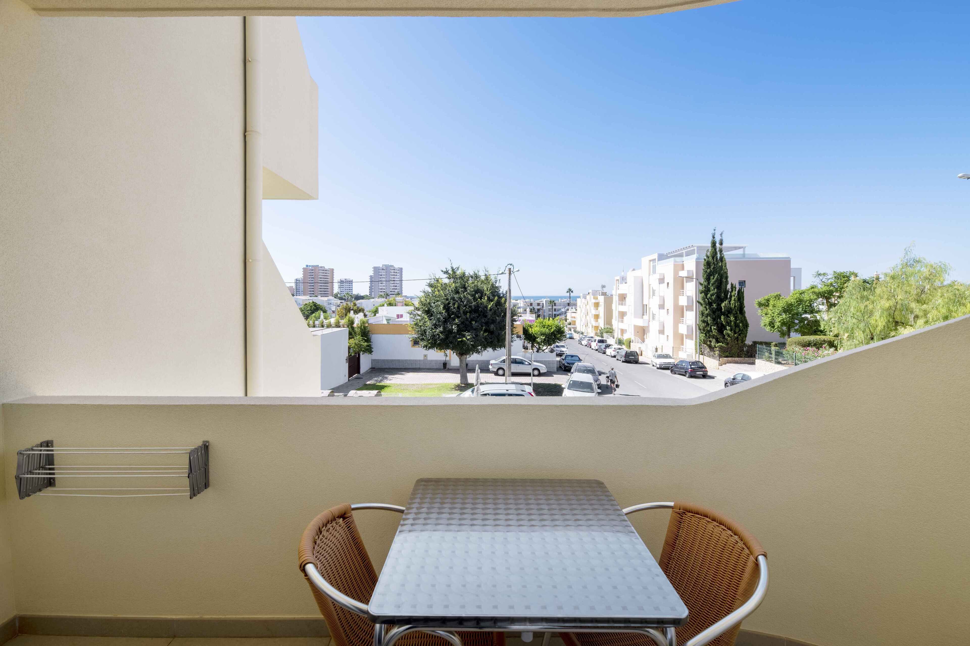 Un balcón con mesa y sillas, con vista a una calle con coches aparcados y edificios.